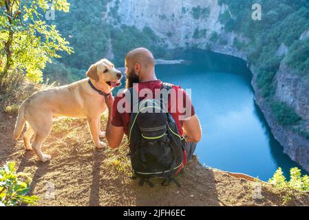 Un routard assis au bord d'une falaise avec son chien Banque D'Images