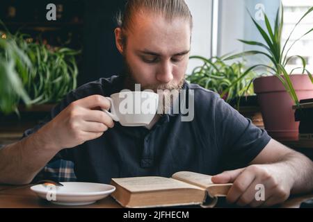 Un jeune homme lit un livre sur une tasse de thé dans un café. Banque D'Images