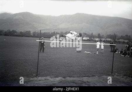 1954, historique, à l'extérieur dans un champ sportif, un garçon faisant le saut en hauteur, bondissant au-dessus des pieds de la barre d'abord avec un bac à sable en dessous, Écosse, Royaume-Uni. Banque D'Images