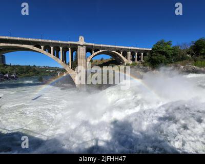 Écoulement torrentiel au-dessus des chutes de Lower Spokane dans le centre-ville de Spokane après de fortes pluies le matin d'été ensoleillé avec arc-en-ciel et le pont de Monroe Street Bridge. Banque D'Images