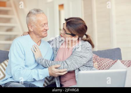 Inquiète femme sénior aimante assise sur un canapé et embrassant son mari tout en lui posant des questions sur la santé Banque D'Images