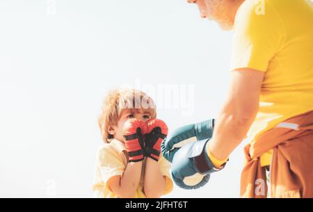 Grand-père et petit-fils combattant en bonne santé avec des gants de boxe. Drôle mignon lutte d'enfant. Drôle d'homme barbu - grand-père avec enfant garçon debout dans la boîte Banque D'Images