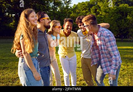 Une compagnie de jeunes amis joyeux et bruyants qui se détendent ensemble à pied en été dans un parc verdoyant. Banque D'Images