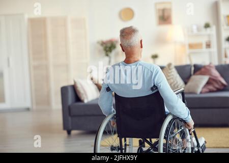 Vue arrière de l'homme âgé à cheveux gris dans un chandail décontracté en fauteuil roulant manuel à la maison Banque D'Images