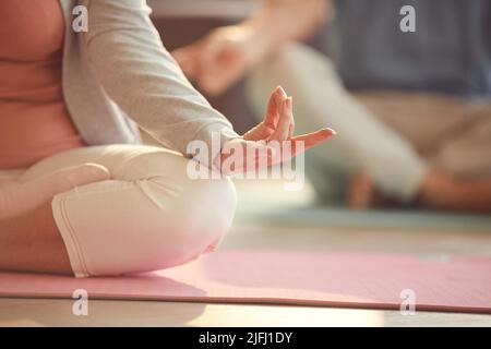 Gros plan d'une femme bâbord méconnaissable assise avec des jambes croisées sur le tapis et tenant la main dans la mudra tout en méditant Banque D'Images