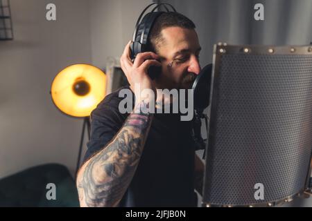 un jeune chanteur tatoué enregistre de la musique à l'aide d'un microphone et d'un casque espace de copie de prise de vue moyenne . Photo de haute qualité Banque D'Images