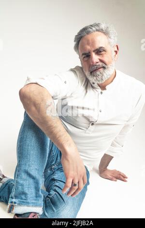 Homme caucasien à poil gris assis en studio, regardant la caméra arrière-plan blanc espace de copie isolé à l'intérieur . Photo de haute qualité Banque D'Images