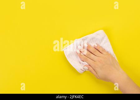 La main d'une femme au foyer tient un chiffon pour épousseter ou laver. Espace vide pour le texte ou le logo sur fond jaune. Début du printemps ou nettoyage régulier. Nettoyage Banque D'Images