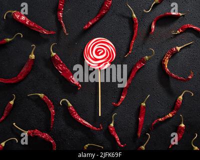 Bonbon rond rouge et blanc tourbillonnant avec piments rouges secs sur fond noir. Contraste des aliments chauds et sucrés. Banque D'Images