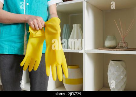 Gros plan de la femme de ménage mettant des gants en caoutchouc jaune avant de nettoyer la pièce Banque D'Images