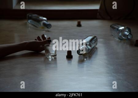 Une main de femme se trouve sur le sol et à côté il y a une bouteille et un verre dans un appartement dans l'obscurité, l'alcoolisme et la consommation, une mauvaise habitude, femme alco Banque D'Images