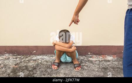 Un doigt pointant vers un enfant s'assoit sur le sol et un petit garçon asiatique se triste Banque D'Images