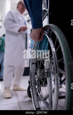 Gros plan de la main d'un homme âgé utilisant un fauteuil roulant devant un médecin pour un rendez-vous à la réception privée de l'hôpital. Accent sélectif sur l'homme âgé vivant avec un handicap à la clinique médicale. Banque D'Images