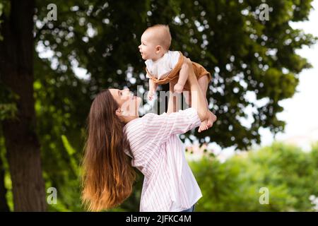 Photo d'excitée gaie mère petit fils habillé décontracté vêtements levant les bras appréciant le soleil à l'extérieur arrière-cour Banque D'Images