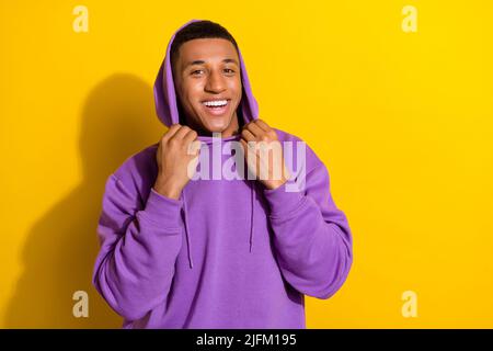 Photo de gai beau jeune homme en violet confortable sweat à capuche aller à pied pendant les vacances d'été isolé sur fond jaune Banque D'Images