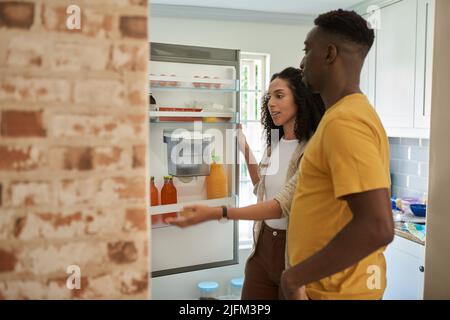 Jeune couple multiethnique à la recherche de quelque chose dans leur réfrigérateur de cuisine Banque D'Images