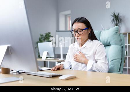 Jeune belle asiatique employée de bureau fatiguée et malade ayant de graves douleurs à la poitrine et des problèmes respiratoires panique attaque femme d'affaires. Banque D'Images