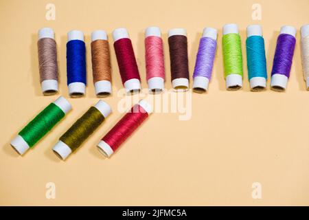 Ensemble de fils multicolores pour la couture avec un espace vide pour le texte sur fond beige, vue de dessus. Équipement de tailleur et de travaux d'aiguille, interdiction sur mesure Banque D'Images