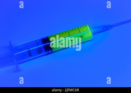 Seringue médicale avec liquide vert sur fond bleu. Vaccin contre la varicelle et le virus corona. Traitement médical. Banque D'Images