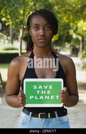 Jeune activiste afro-américain avec un message sauver la planète sur un écran de tablette. Banque D'Images