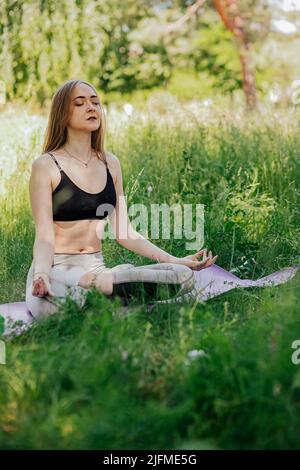 Femme de yoga sur l'herbe verte fille se détend dans le champ. Femme de yoga dans le parc vert fille faisant de la gymnastique à l'extérieur. Méditer la femme dans la méditation dans le yoga pose pratiques à l'extérieur Banque D'Images
