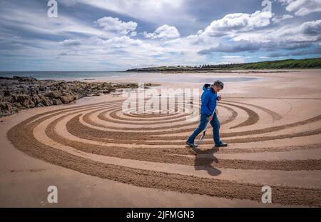 L'artiste Sean Corcoran, originaire de Waterford, en Irlande, crée un morceau d'art du sable sur la plage de Tyninghame, Lothian oriental, pendant le Festival d'art terrestre européen de Lothian oriental. Le Festival est un événement d'une semaine qui comprend des artistes de la nature du monde entier qui créent des dessins de sable, des sculptures en bois et des piles de pierre en utilisant uniquement des matériaux trouvés le long de la côte. Date de la photo: Lundi 4 juillet 2022. Banque D'Images