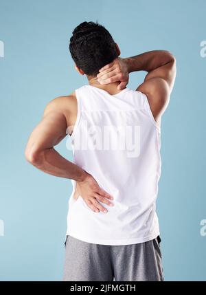 Jeune homme de course mixte, à la vue arrière, portant une veste en studio isolée sur fond bleu. Athlète masculin méconnaissable souffrant de douleurs dorsales ou Banque D'Images