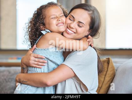 Une mère aimante et une fille qui s'embrassent les uns les autres en partageant un câlin tout en étant assis sur le canapé à la maison. Un parent affectueux et un enfant partageant un moment d'appel Banque D'Images