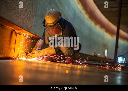 Homme travailleur métal coupure étincelle sur la plaque en acier du fond du réservoir avec flash de la lumière de coupe gros plan porter des gants de protection et un masque dans un espace confiné latéral Banque D'Images