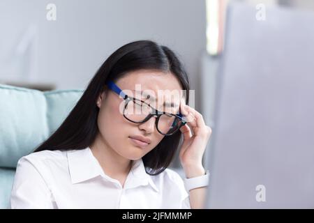 Photo en gros plan d'une femme d'affaires fatiguée au bureau, d'une femme asiatique tenant les mains sur la tête, ayant de graves maux de tête et de la fatigue Banque D'Images