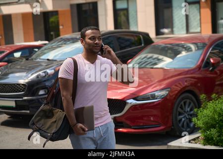 Homme avec ordinateur portable parlant sur smartphone dans le parking Banque D'Images