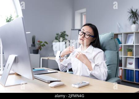 Chaleur dans le bureau, femme asiatique essayant de se rafraîchir, femme d'affaires travaillant à l'ordinateur, en agitant ses mains pour se refroidir. Banque D'Images