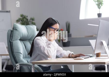 Une employée de bureau asiatique malade, a le froid et la grippe, tousse et éternue dans les tissus, travaille à l'ordinateur. Banque D'Images