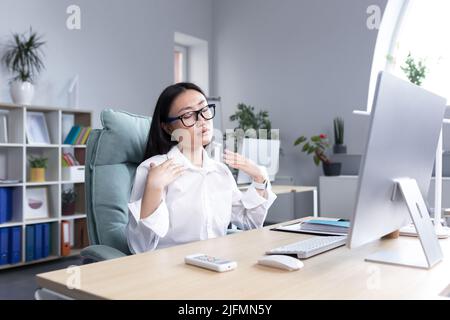 Chaleur dans le bureau, femme asiatique essayant de se rafraîchir, femme d'affaires travaillant à l'ordinateur, en agitant ses mains pour se refroidir. Banque D'Images