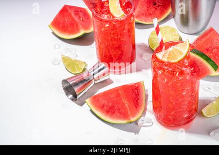 Cocktail de limonade au melon d'eau avec citron vert et tranches de pastèque, sur fond de papier rose blanc de couleur tendance Banque D'Images