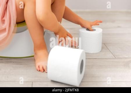 Un enfant sur le pot joue avec du papier toilette. Banque D'Images