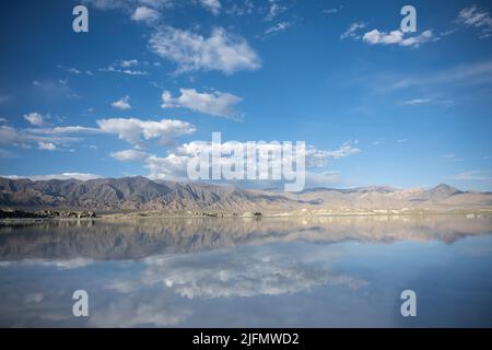 Une côte montagneuse et le ciel avec plusieurs nuages parfaitement reflétés dans un lac Banque D'Images