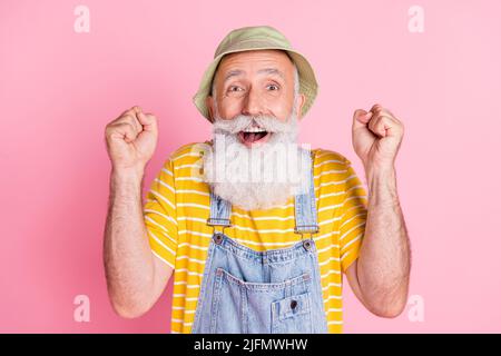 Photo de gai excitée fou mature homme porter chapeau de soleil lève les poings dans le triomphe isolé sur fond de couleur rose Banque D'Images