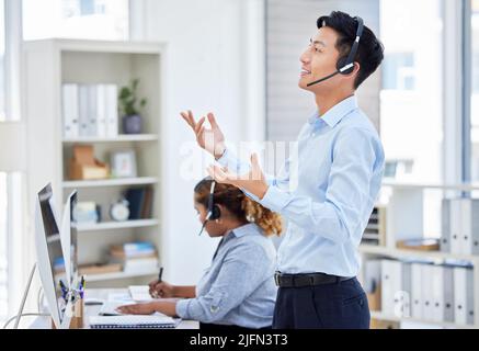 Un représentant du service client asiatique confiant se tient debout et parle sur un micro-casque au bureau. Homme travaillant dans le conseil de centre d'appels et exploitant un service d'assistance pour Banque D'Images