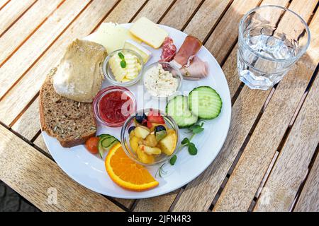 Petit déjeuner ou déjeuner avec petits pains, fromage, saucisses et fruits sur une table extérieure en bois, par beau temps, sélection, champ étroit Banque D'Images