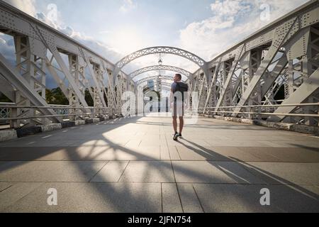 Vue arrière de l'homme avec sac à dos tout en marchant sur le pont historique en acier dans le centre-ville de Singapour. Banque D'Images