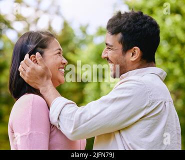 Un mari aimant qui met les cheveux derrière une oreille debout face à face dans un parc. Heureux moments romantiques de couple charmant passer du temps ensemble à l'extérieur Banque D'Images