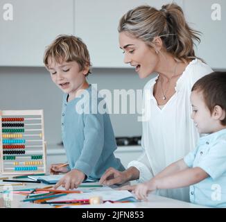 Mère caucasienne aidant son enfant à faire ses devoirs. Maman fière regardant les dessins des enfants en apprenant sur les couleurs. Jeune mère à la maison avec deux fils. Enfants Banque D'Images