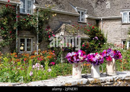 Un joli jardin de cottage anglais en pleine fleur par jour ensoleillé. Des fleurs coupées en cruches sont placées sur le mur du jardin sur une toile de fond de plantes traditionnelles Banque D'Images