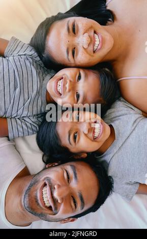 Portrait d'une famille de quatre personnes en pyjama, couchée ensemble sur un lit en souriant et en prenant des selfies amusants à la maison. Parents aimant Banque D'Images