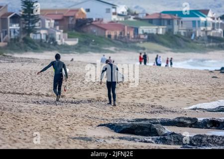 Une vue arrière des surfeurs en combinaisons marchant sur la plage avec des planches de surf à Jeffreys Bay, Afrique du Sud Banque D'Images