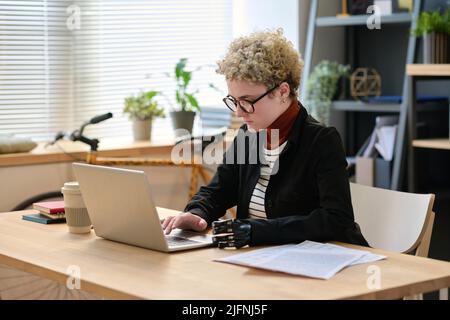 Jeune femme avec un bras prothétique tapant sur un ordinateur portable travaillant sur son lieu de travail au bureau Banque D'Images