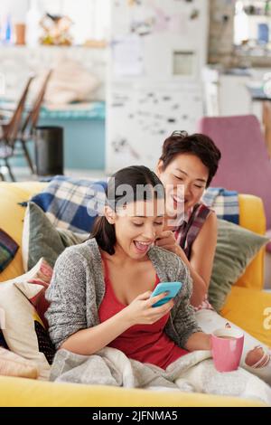 Regarde ce qui se trouve dans mon système de gestion des concessionnaires. Photo d'une femme regardant quelque chose sur son téléphone portable tandis que son ami fait ses cheveux. Banque D'Images