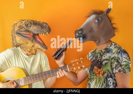 Amis heureux ayant plaisir à jouer de la guitare et à boire de la bière portant des masques de tête d'animal isolé sur fond orange.Party couple amis, concep surréaliste Banque D'Images