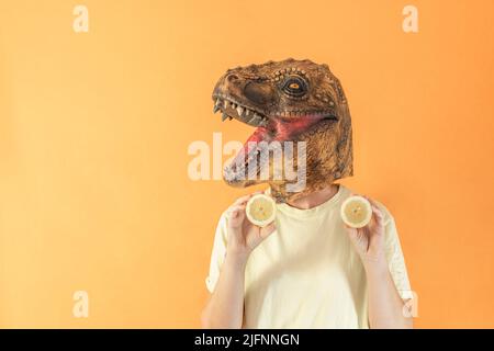 Femme dans un masque de tête de dinosaure tenant des tranches de citron frais sur fond orange Banque D'Images